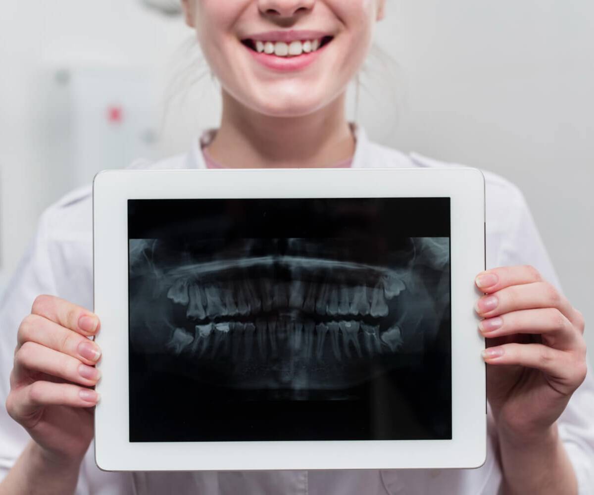 In the image, a dentist shows a patient's dental digital radiograph with a tablet in his hand