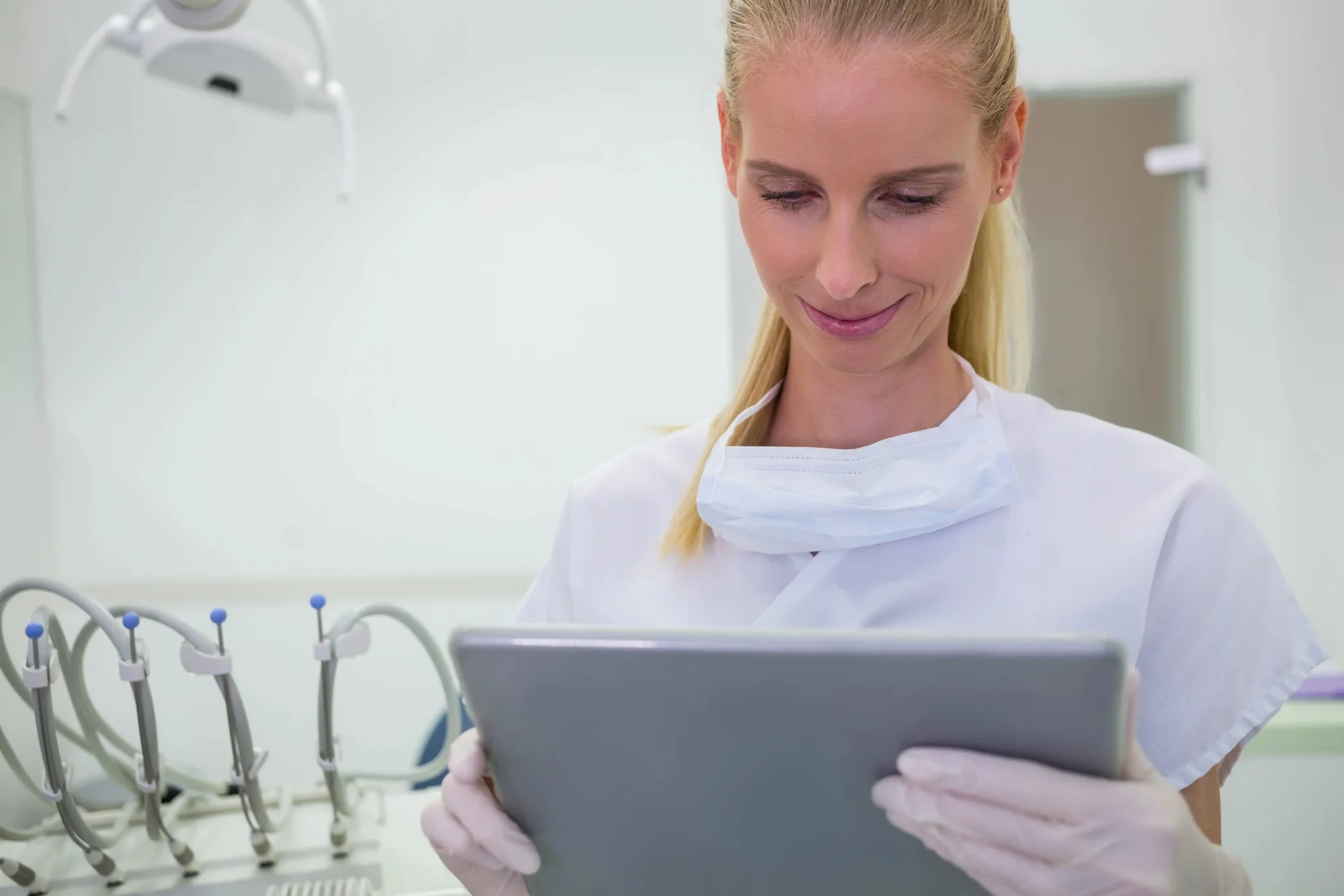 Female dentist in a white coat, wearing a dental mask and working on a tablet.