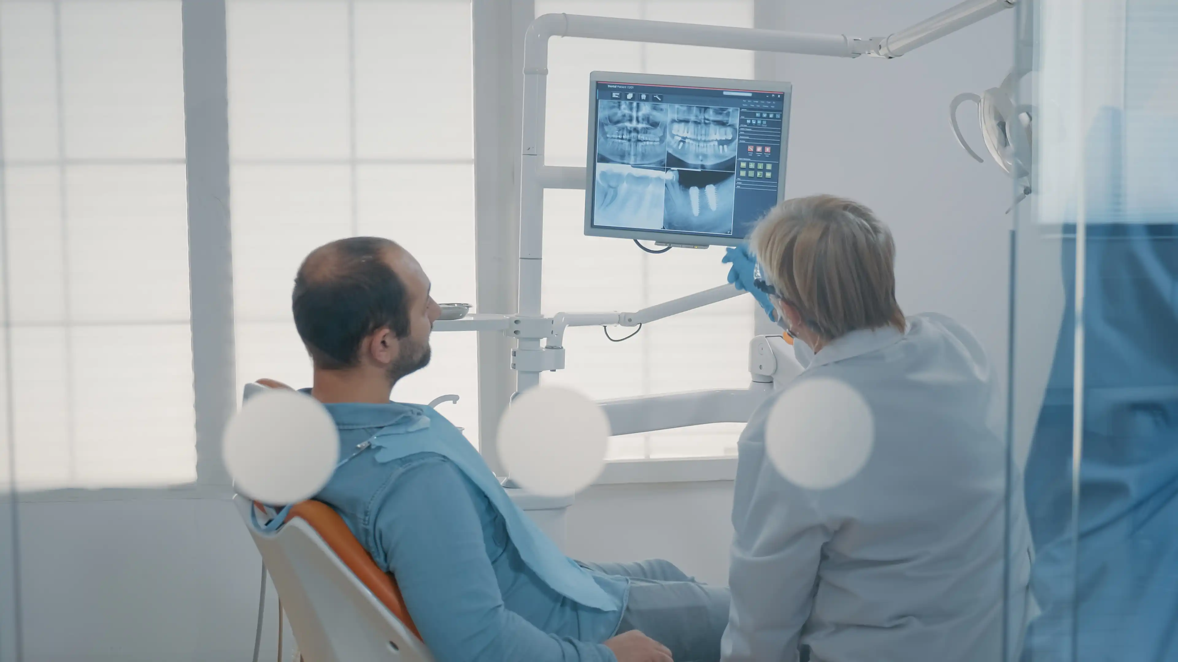 An experienced dentist providing a second opinion, explaining a dental diagnosis using an X-ray to a patient.